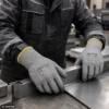 Metalliteollisuuden työntekijä käyttää PROGLO PU-pinnoitettuja D-luokan viiltosuojakäsineitä metalliosien käsittelyssä.