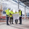 Rakennustyömaan työntekijät tarkastelemassa piirustuksia suojataskussa